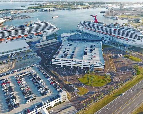 Aerial photo of Canaveral Port Authority Cruise Terminal 5. Two cruise ships in port. One of the ships is docked at the new two-story passenger and baggage handling areas. Large parking garages.